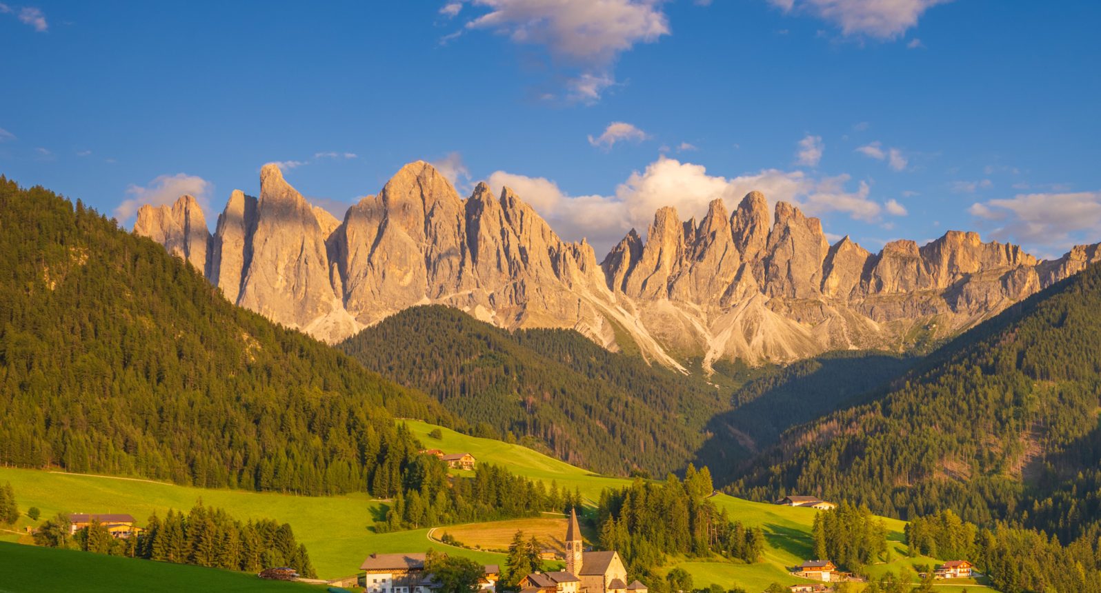 Santa Maddalena church in Val di Funes at sunset, with the Odle peaks of the Dolomites glowing above green meadows