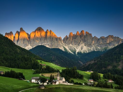 Santa Maddalena church in Val di Funes at sunset, with the Odle peaks of the Dolomites glowing above green meadows